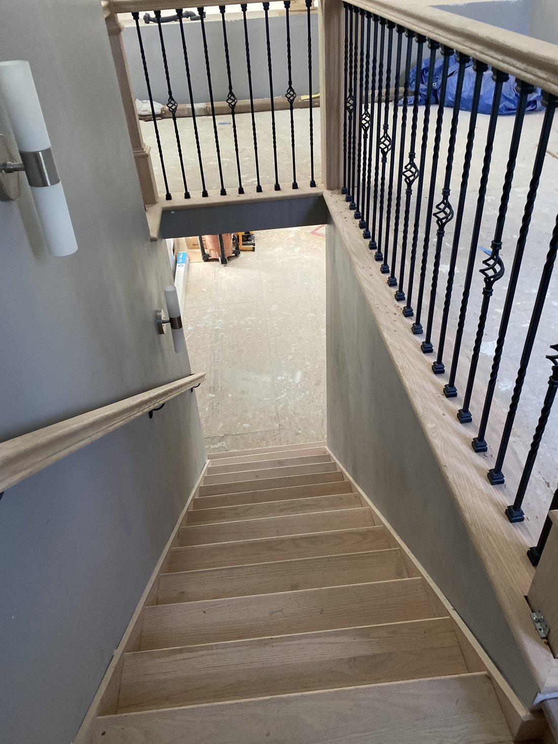 Oak stair treads and railing with black iron balusters leading down to the lower level